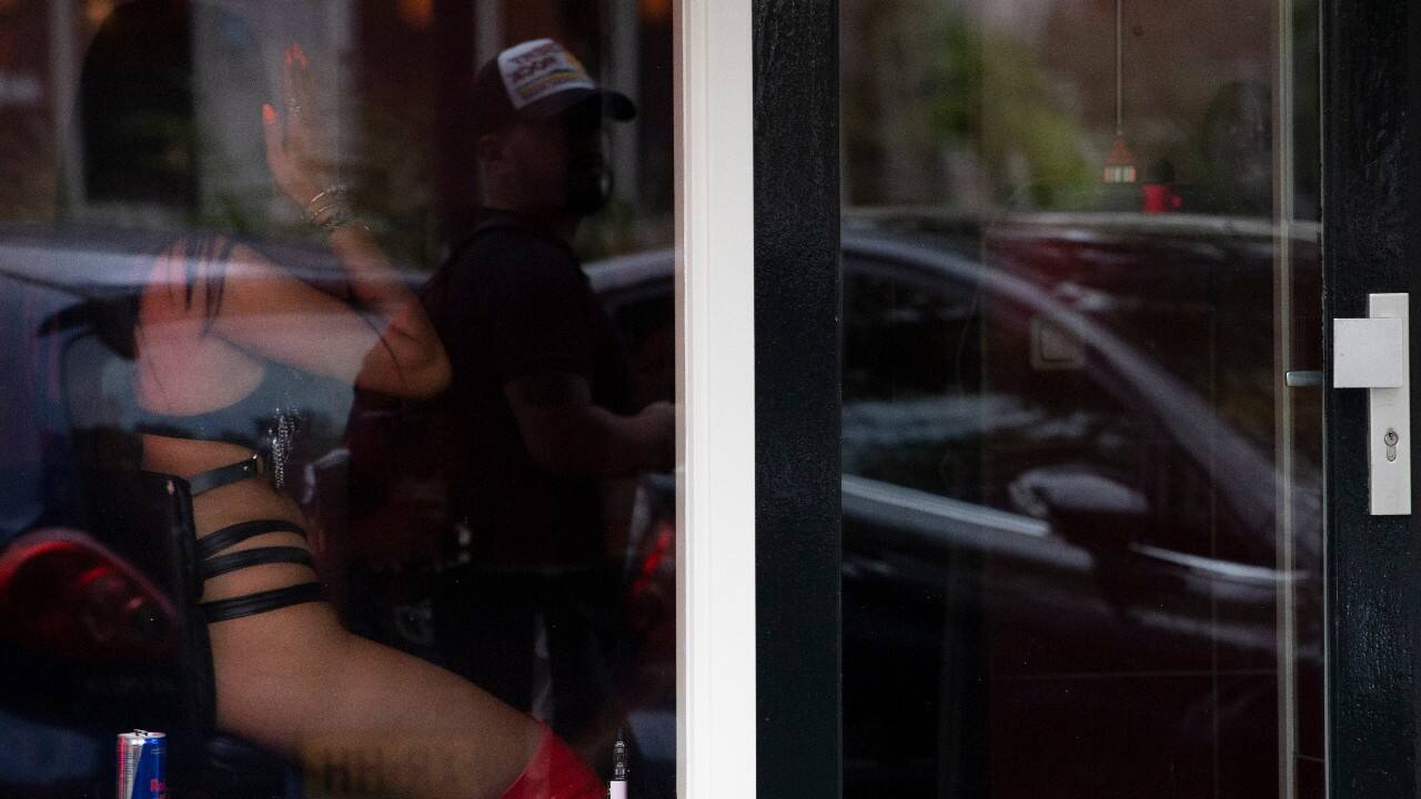 A sex worker shields her face from the photographer as a passing man is reflected in the window after a further ease of corona virus restrictions in Amsterdam, Netherlands, July 1. Sex workers at the cobbled streets and canals where they pose in windows bathed in red light to attract customers, are taking care of hygiene to minimize the risk to themselves and their clients of becoming infected with the coronavirus. (AP Photo/Peter Dejong)