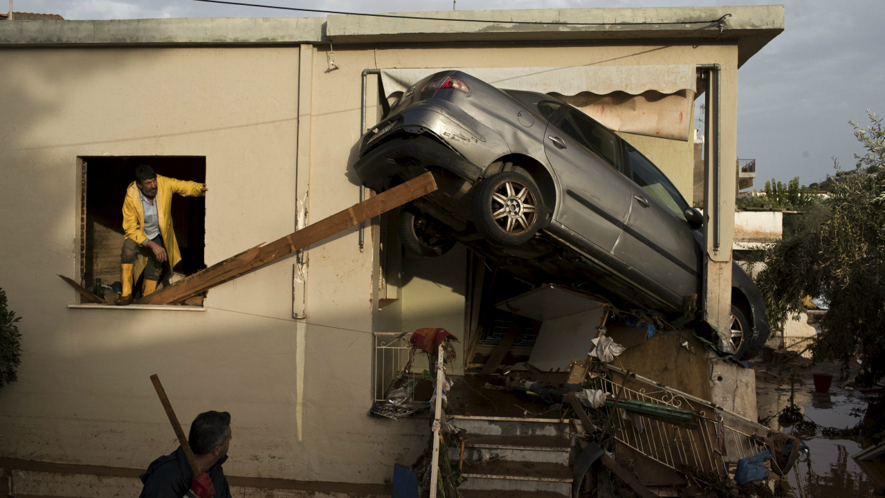 Workers try to remove a flipped over car at the entrance of a house in the town of Mandra western Athens, Greece. (AP)