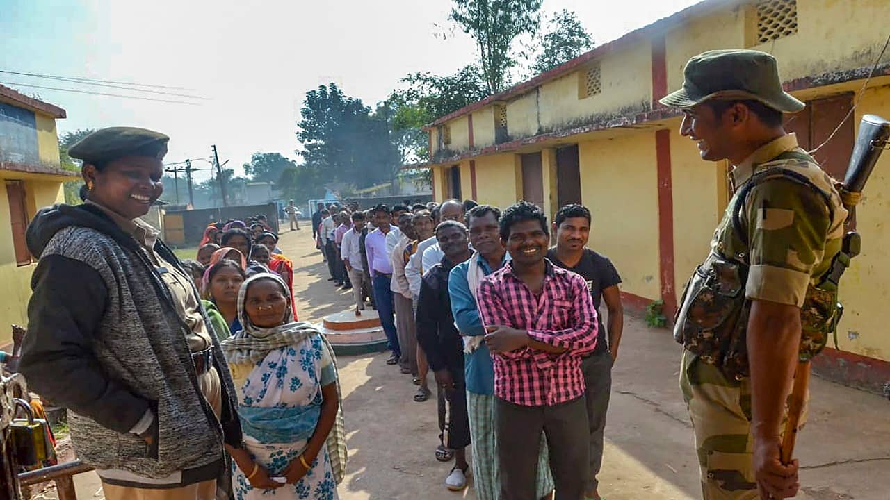 Security personnel stand guard as people wait in queues to cast their votes at a polling station at Mangnar in Naxal-affected Bastar district during the first phase of Assembly elections. (Image: PTI)