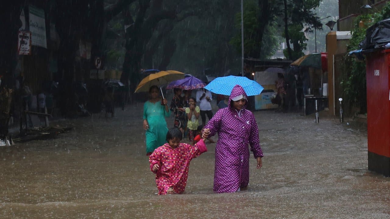 Mother and child wade through a waterlogged street in the city. (Image: AP)