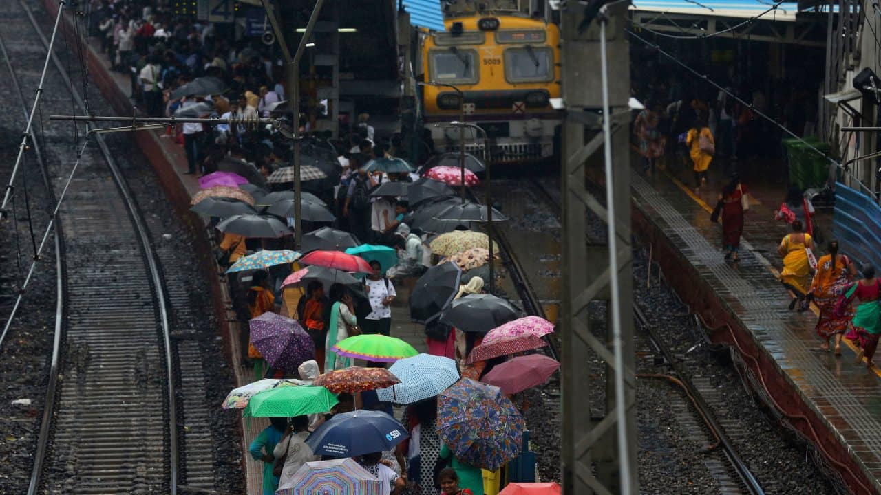 As trains are getting delayed, people hold umbrellas as they wait at a station. (Image: AP)