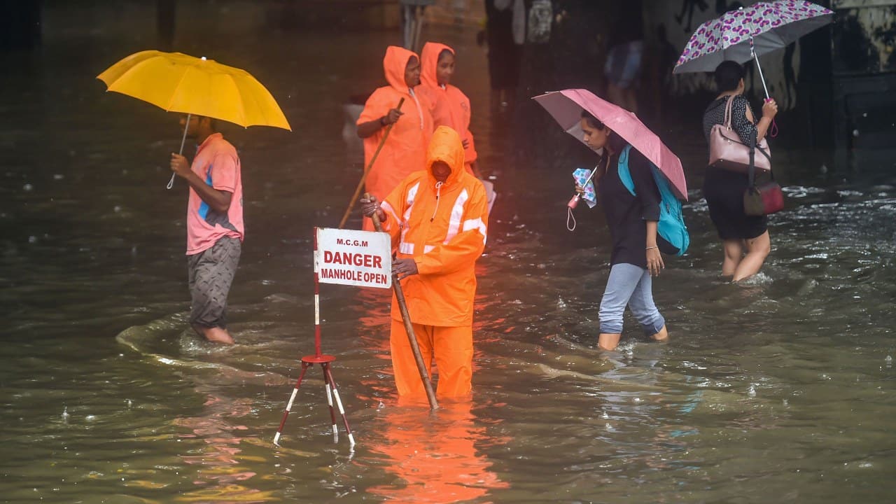 A Municipal worker stands guard to warn pedestrians of an open manhole on a waterlogged street following heavy monsoon rains, in Mumbai on July 01, 2019. (Image: PTI)