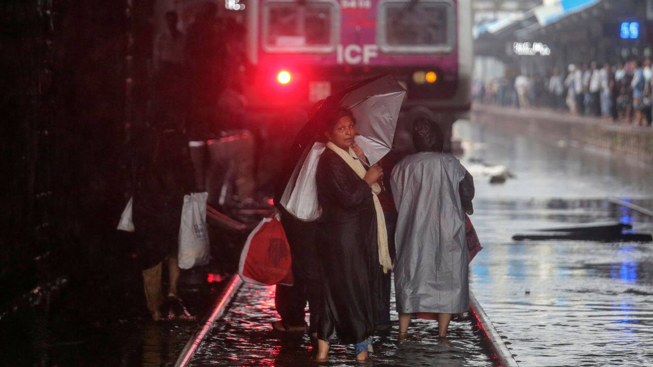 Commuters cross waterlogged railway tracks as a suburban train is seen parked at a railway station after its services were suspended during heavy monsoon rains. (Image: Reuters)