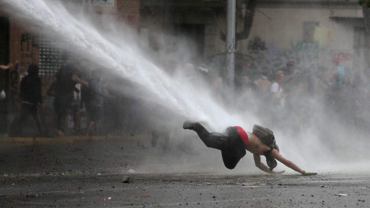 A demonstrator dives to the ground from a water cannon during a protest against Chile's government in Santiago, Chile on November 11, 2019. (Image: Reuters/Ivan Alvarado)