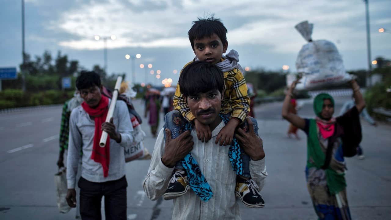 A migrant worker carries his son as they walk along a road with others to return to their village from New Delhi. (Image: Reuters)