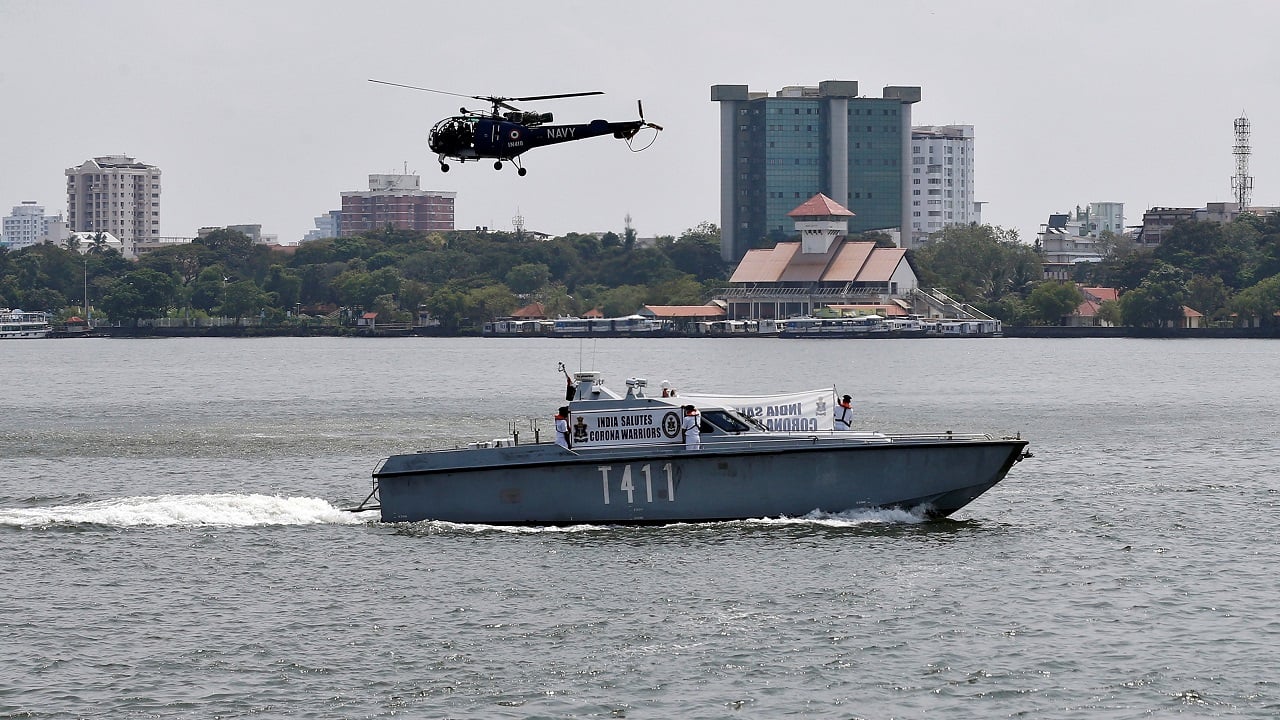 Indian Navy soldiers display a banner on a Fast Interceptor Crafts (FIC) boat in the waters of Vembanad Lake as a Chetak helicopter flies past, in Kochi, Kerala. (Image: Reuters)