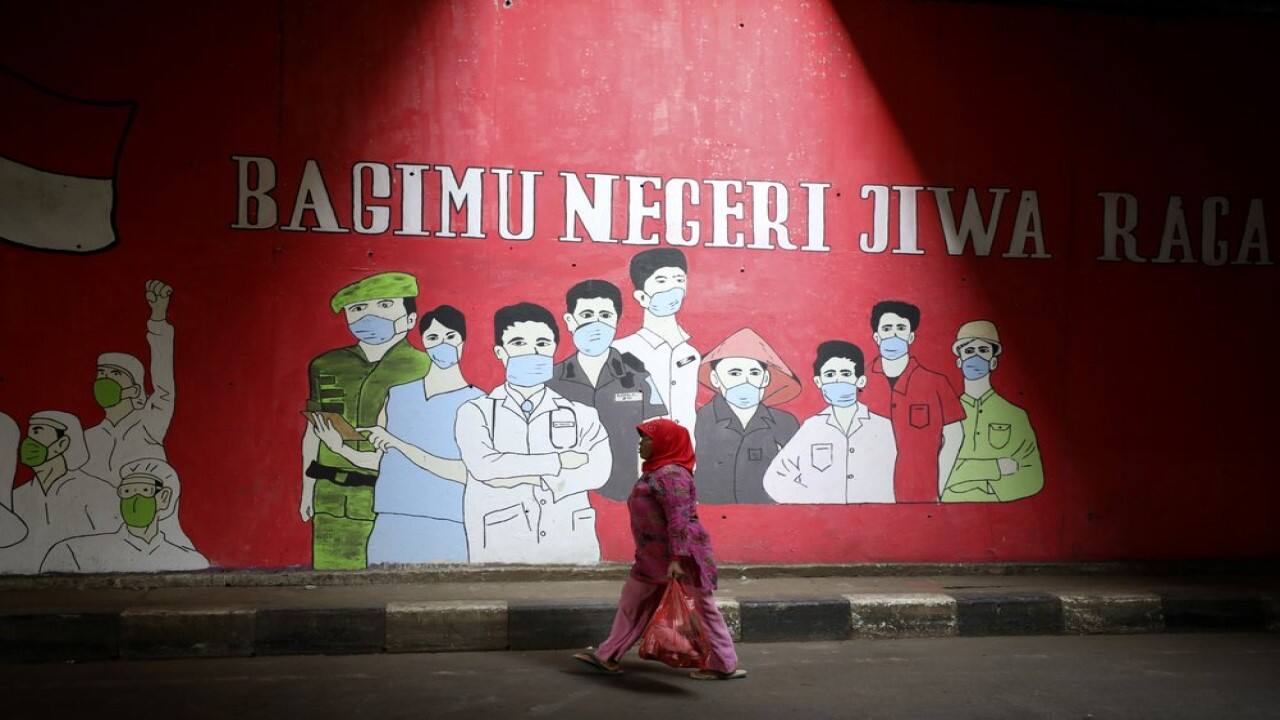 A woman walks past a coronavirus-themed mural honoring health and other essential workers, in Jakarta, Indonesia, Wednesday, Aug. 26, 2020. Writings on the mural read: &quot;Our body and soul for the country.&quot; (Image: AP Photo/Dita Alangkara)