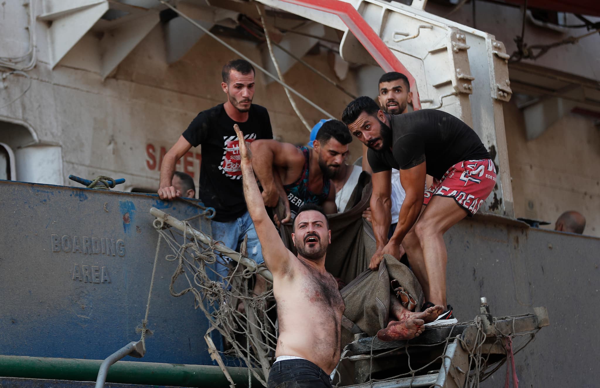 Civilians help to evacuate an injured sailor from a ship which was docked near the explosion scene that hit the seaport of Beirut, Lebanon, Tuesday, Aug. 4, 2020. (AP Photo/Hussein Malla)