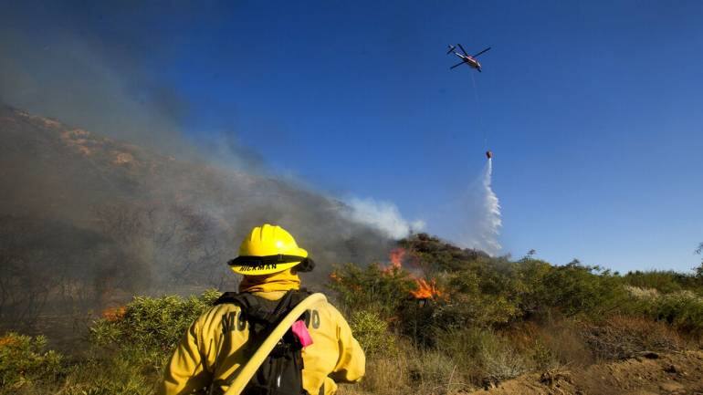 A firefighter watches as a helicopter drops water onto the Apple Fire nearing Banning, California (Image Courtesy: AP)