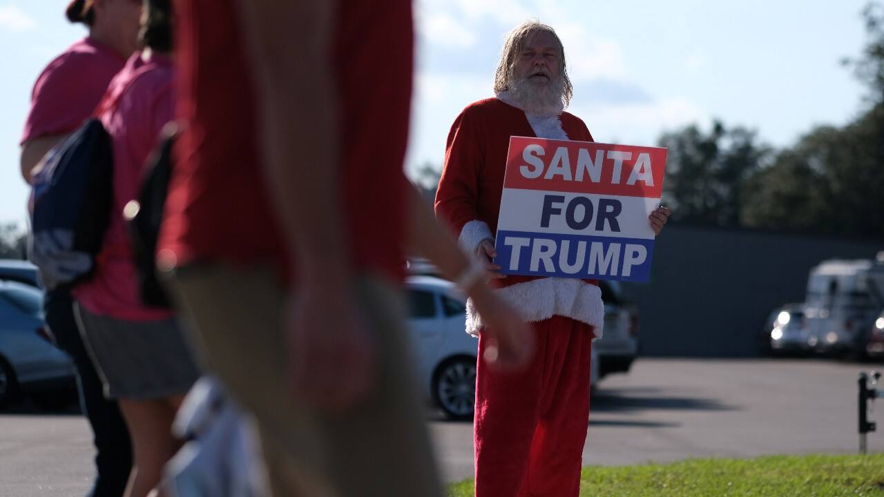 A man dressed as Santa Claus holds a sign as supporters of U.S. President Donald Trump arrive for an election campaign rally at Orlando Sanford International Airport in Sanford, Florida, U.S. October 12. (Image: Reuters)