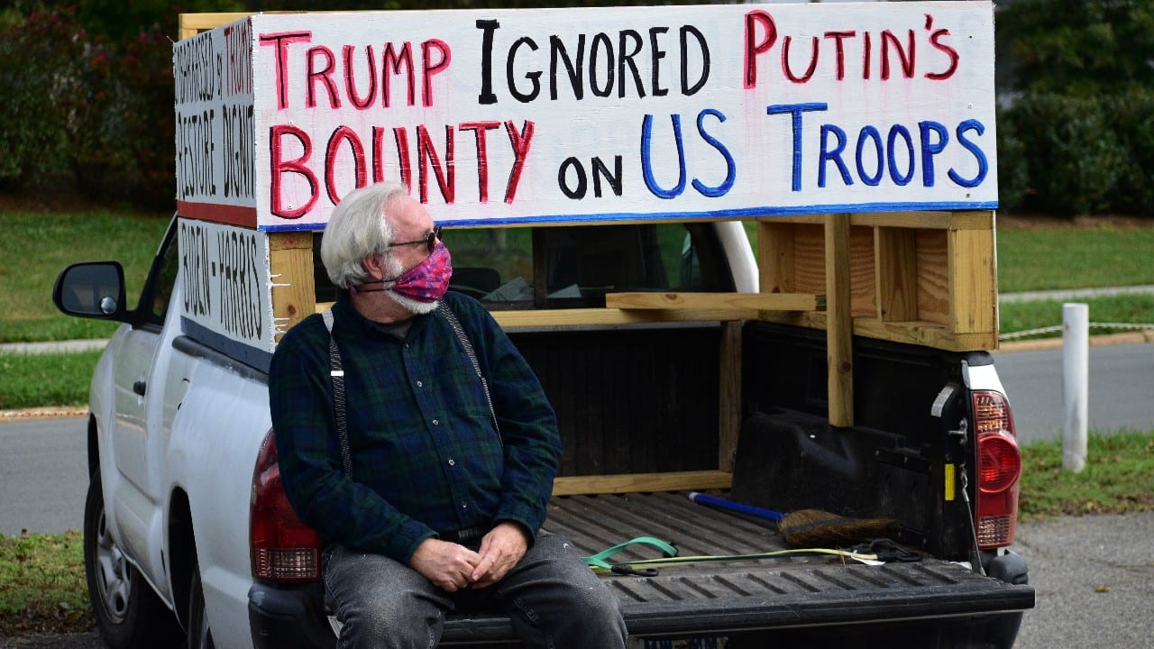 A man sits near a sign referring to U.S. President Donald Trump and Russian President Vladimir Putin before a Get Out The Vote march in Graham, North Carolina, U.S. October 31. (Image: Reuters)
