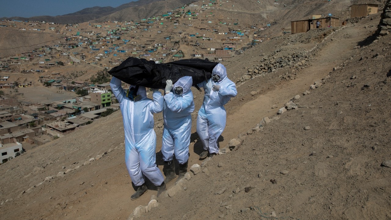 Venezuelan migrants Luis Zerpa leads Luis Brito and Jhoan Faneite to carry the remains of 51-year-old Marcos Espinoza who is suspected fo dying of the new coronavirus, down a steep hill to a waiting hearse in a working-class neighborhood near Pachacamac, the site of an Inca temple, on the outskirts of Lima, Peru, May 8. (Image: AP)
