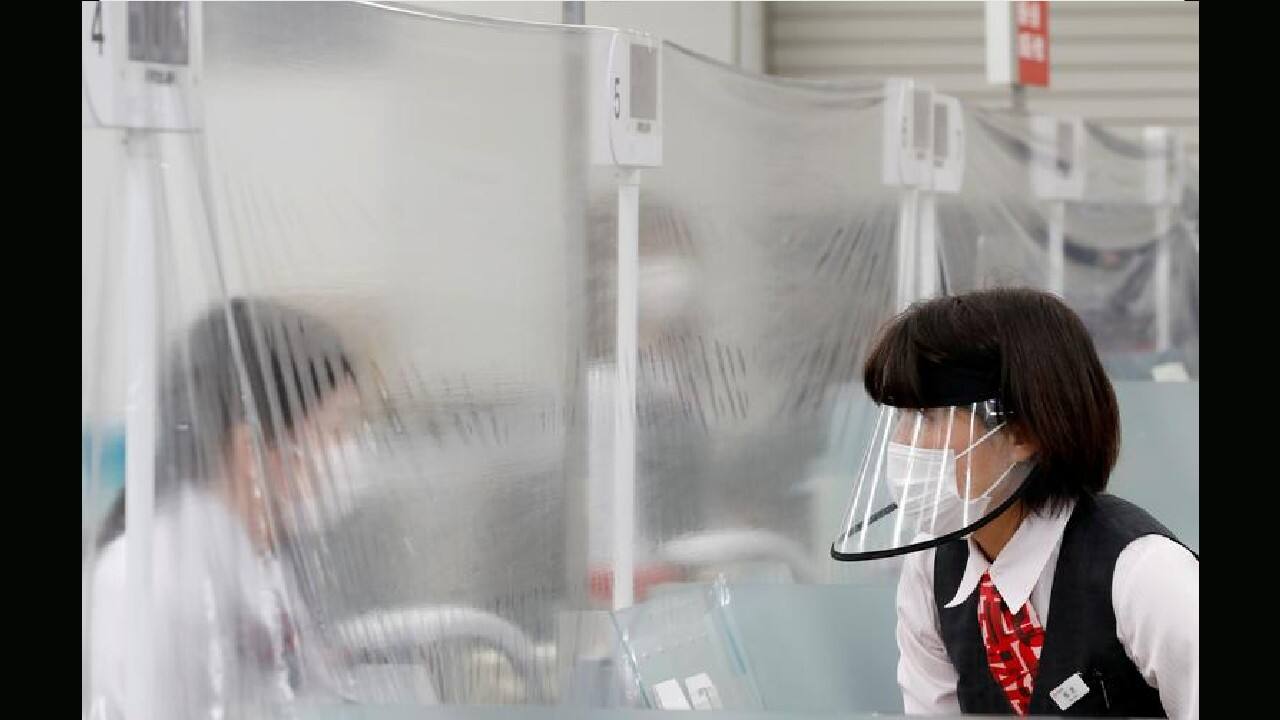 A staff member wearing a face shield talks to a bank teller at a counter where a plastic curtain is installed in a branch of MUFG Bank in Tokyo, Japan, April 24. (Image: Reuters) A staff member wearing a face shield talks to a bank teller at a counter where a plastic curtain is installed in a branch of MUFG Bank in Tokyo, Japan, April 24. (Image: Reuters)