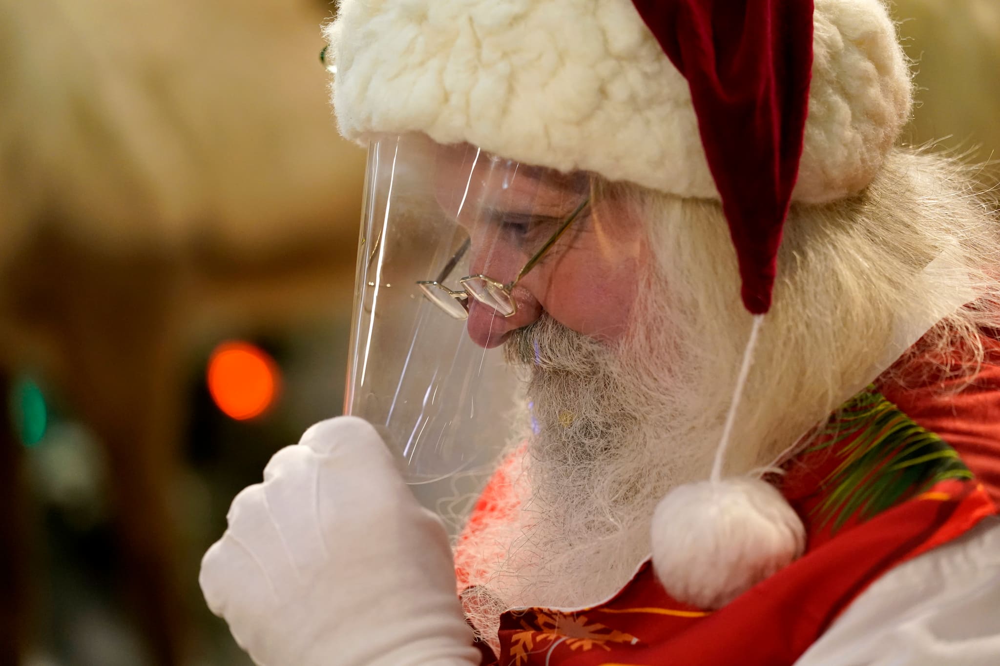 Santa Claus adjusts his protective face shield between visits from children and their families at Bass Pro Shops, in Miami on Nov. 20, 2020. In this socially distant holiday season, Santa Claus is still coming to towns (and shopping malls) across America but with a few 2020 rules in effect. (AP Photo/Lynne Sladky)