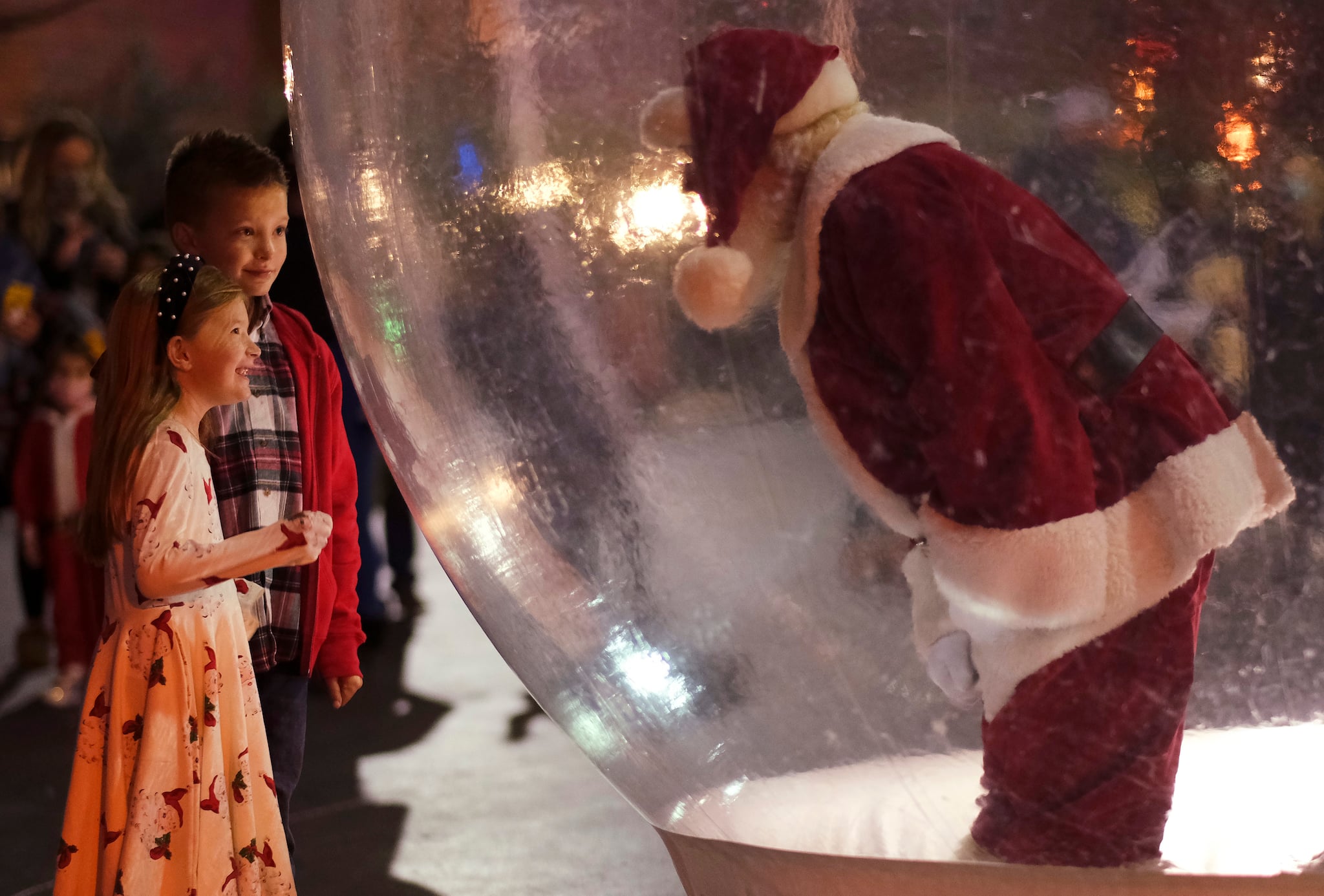 A young girl and boy visit with the Santa in a snow globe during Automobile Alley's Lights on Broadway in Oklahoma City, Okla., Saturday, Dec. 5, 2020. In this socially distant holiday season, Santa Claus is still coming to towns (and shopping malls) across America but with a few 2020 rules in effect. (Doug Hoke/The Oklahoman via AP)