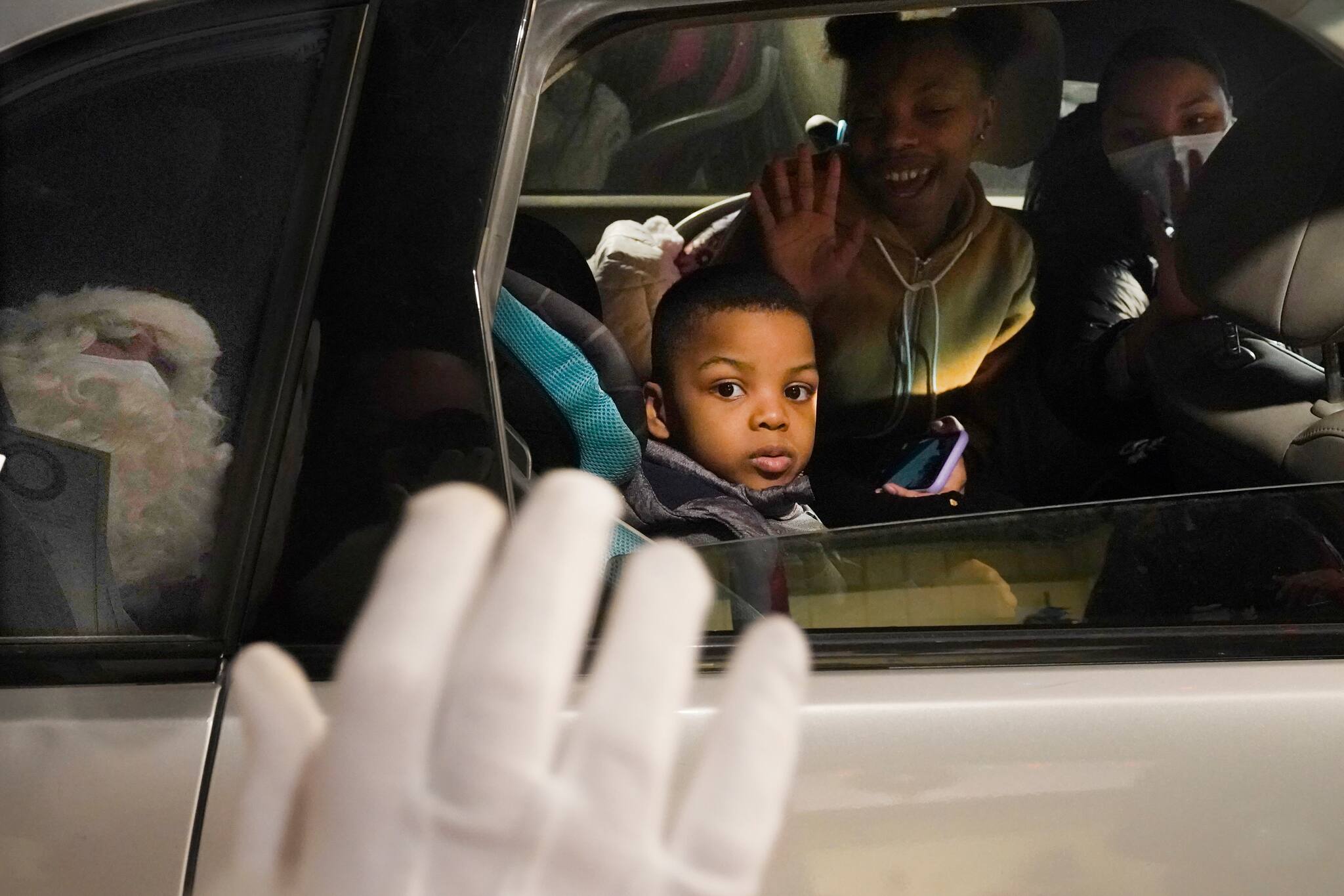 A young boy watches as a reflected, social distant Santa waves while visiting Santa's Garage on top of a parking deck near Soldier Field in Chicago on Dec. 10, 2020. In this socially distant holiday season, Santa Claus is still coming to towns (and shopping malls) across America but with a few 2020 rules in effect. (AP Photo/Charles Rex Arbogast)