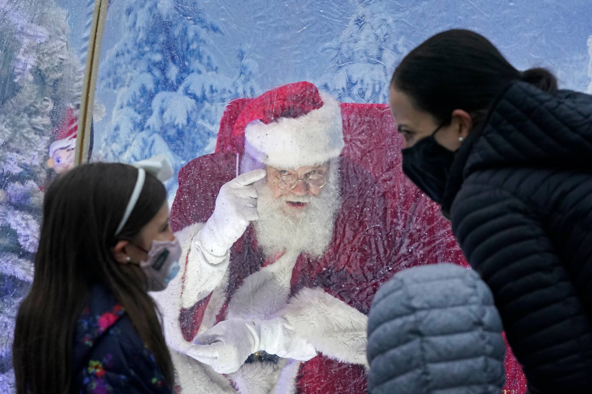 Santa, portrayed by Dan Kemmis, talks to a family wearing masks as he sits inside a protective bubble in Seattle's Greenwood neighborhood on Dec. 8, 2020. Kemmis has been Santa in past years, but he started his daily appearances early this year and added his &quot;snow globe&quot; tent due to the Coronavirus pandemic. In this socially distant holiday season, Santa Claus is still coming to towns (and shopping malls) across America but with a few 2020 rules in effect. (AP Photo/Ted S. Warren)