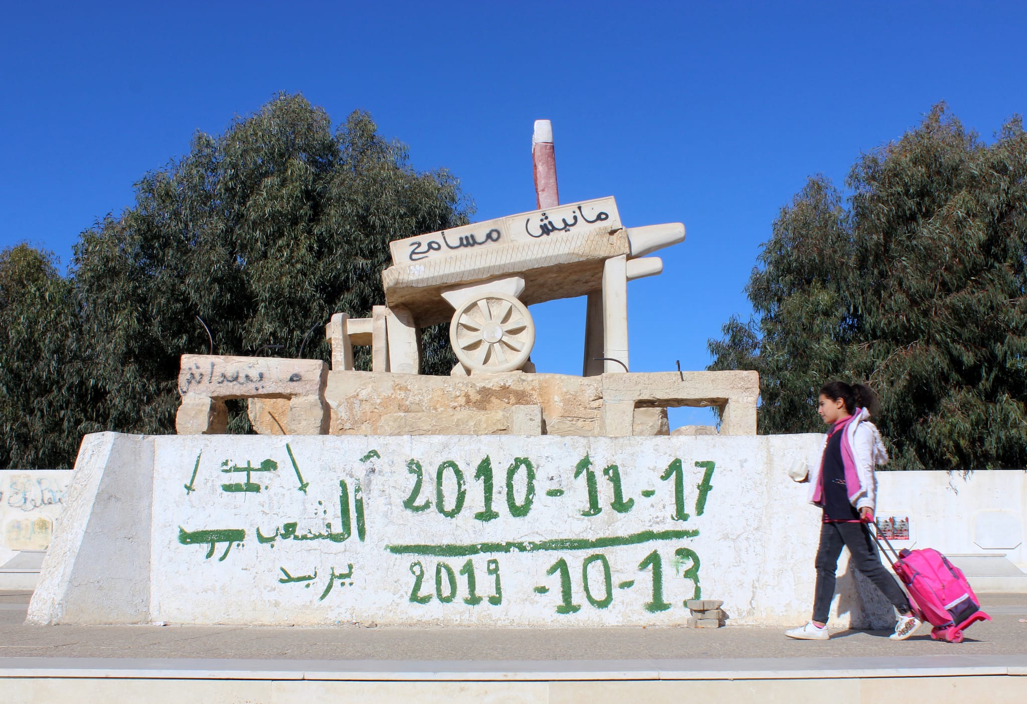 A girl walks past a memorial for Mohamed Bouazizi, a street vendor who set himself alight 10 years ago on December 17, 2010, in Sidi Bouzid, Tunisia December 8, 2020. Graffiti reads: &quot;The people want&quot;. Picture taken December 8, 2020. REUTERS/Angus McDowall - RC2MNK9OQXYL