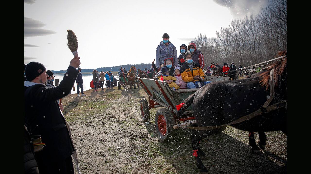 A priest blesses people wearing face masks and their horses during Epiphany celebrations in a field outside the village of Facaeni, on the Danube river banks, southern Romania, January 6. Due to the COVID-19 pandemic, the local traditions which usually include the throwing of a wooden cross in the Danube River that swimmers compete to retrieve after, blessing horses with holy water and a horse race, were drastically reduced by local authorities. (Image: AP/Vadim Ghirda)