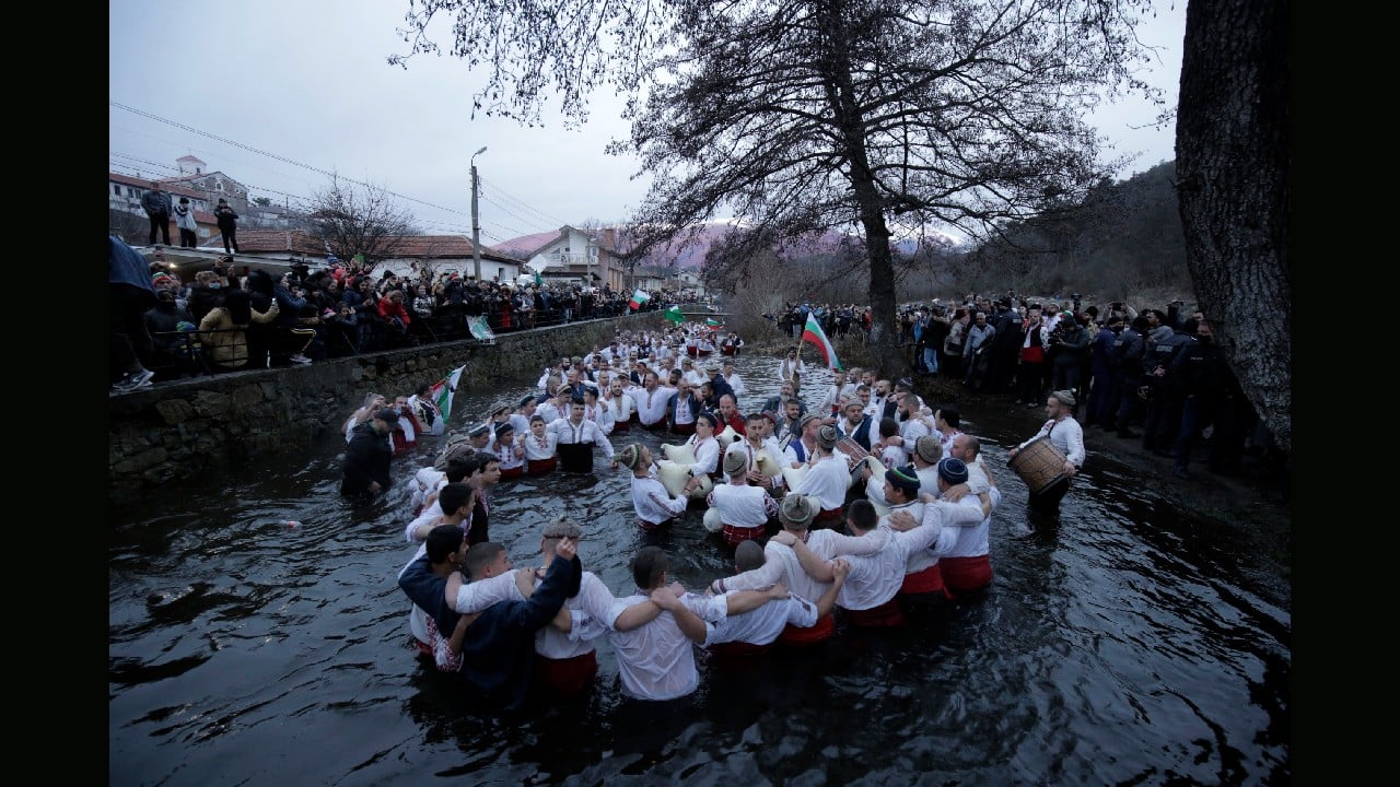 Dozens of residents of the mountain town of Kalofer, central Bulgaria, clad in traditional clothing, stand in the icy Tundzha River, some waving national flags to recover a crucifix cast by a priest in an old ritual marking the feast of Epiphany, January 6. The legend goes that the person who retrieves the wooden cross will be freed from evil spirits and will be healthy throughout the year. (Image: AP/Valentina Petrova)