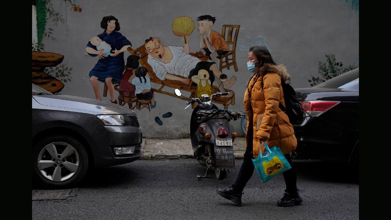 A resident wearing a mask past by a mural depicting idyllic home life in Wuhan in central China's Hubei province on January 15. (Image: AP)