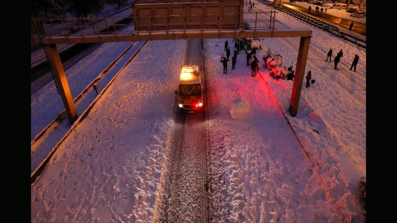 An emergency vehicle drives past people walking in the snow on the M-30 motorway, in Madrid, Spain, January 9. (Image: Reuters)