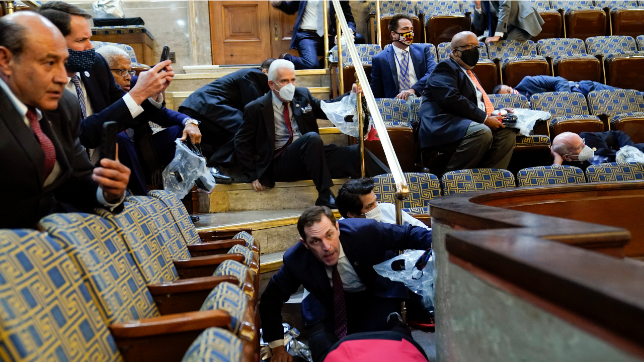 People shelter in the House gallery as protesters try to break into the House Chamber at the US Capitol on January 6, 2021 in Washington. (Image: AP Photo/Andrew Harnik)