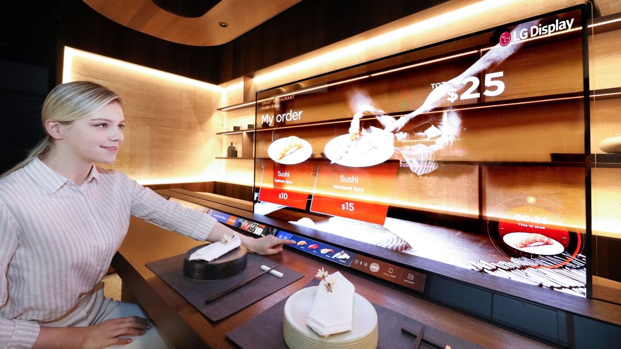  LG also showed off a large 55-inch transparent OLED display and a 23.1-inch in-Touch stretch display for restaurants of the future. In its demo, you can see a customer sitting on one side of the table in a mock sushi bar, while the chef prepares the food right behind the display on the other side. As a dinner, you can browse the menu and order food by using the touchscreen strip on the bottom. Once you’ve placed the order, you can proceed to watch a sporting event or other content on the 55-inch OLED. Because the screen is 40 percent transparent, you can still see the chef preparing your food on the other side. 