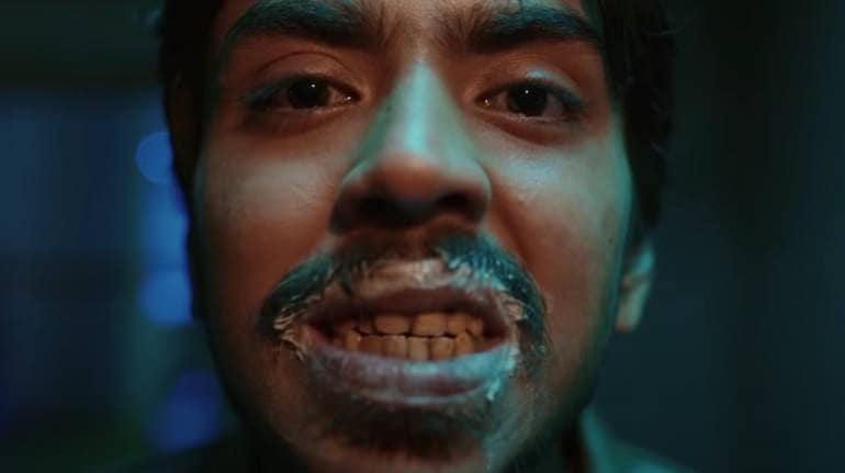 Balram with toothpaste on his lips and grinning into the mirror after brushing his crooked, stained teeth