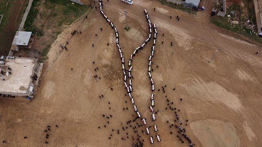 An aerial picture shows mourners carrying coffins wrapped in the Iraqi flag in a procession during a mass funeral for Yazidi victims of the Islamic State (IS) group in the northern Iraqi village of Kojo in Sinjar district, on February 6, 2021. - The remains of 104 Yazidi victims of the Islamic State group have been returned for burial in Kojo, six years after the IS group swept through northern Iraq. (Photo by Zaid AL-OBEIDI / AFP)