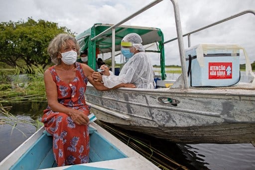 Olga D'arc Pimentel, 72, is vaccinated by a health worker with a dose of Oxford-AstraZeneca COVID-19 vaccine in the Nossa Senhora Livramento community on the banks of the Rio Negro near Manaus, Amazonas state, Brazil on February 9, 2021. (Photo by MICHAEL DANTAS / AFP)