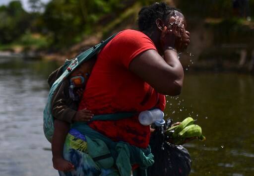 A migrant carrying a baby refreshes in the Chucunaque river after walking for five days in the Darien Gap, in Bajo Chiquito village, Darien province, Panama on February 10, 2021, on their way to the US. - Migrants from Haiti and several African countries remain stranded at the Panama-Colombia border, while the Central American country is expecting a new wave of migrants. (Photo by Luis ACOSTA / AFP)