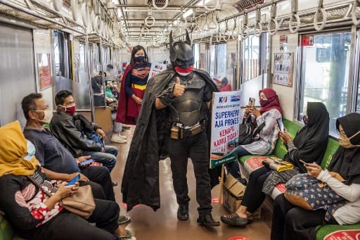 A couple (C) dressed in superhero costumes walk through a commuter train to promote health awareness to prevent the transmission of the COVID-19 coronavirus in Yogyakarta on February 11, 2021. (Photo by AGUNG SUPRIYANTO / AFP)