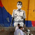 A roadside barber cuts the hair of a man in front of a wall with graffiti in Mumbai