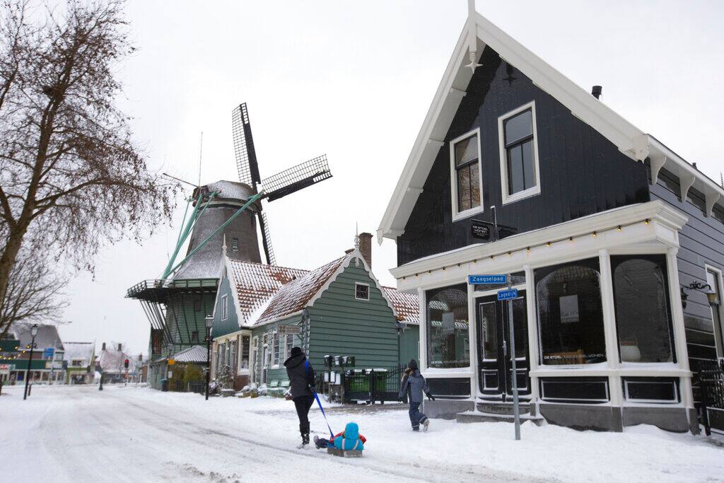 A woman pulls her child on a sled in Zaandam, near Amsterdam, Netherlands, Sunday, Feb. 7, 2021. Snow and strong winds pounded The Netherlands, with more cold and snow expected in the days ahead. (AP Photo/Peter Dejong)