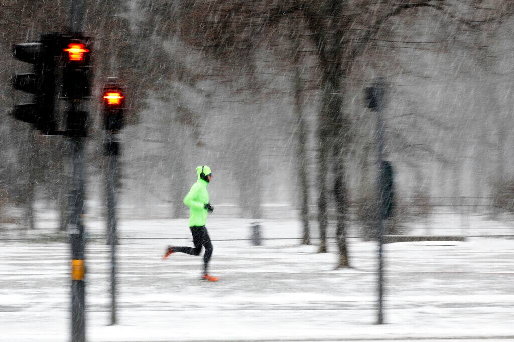 A man runs during snowfall in central Berlin, Germany, Sunday, Feb. 7, 2021. A snowstorm and strong winds pounded parts of Germany on Sunday. (AP Photo/Markus Schreiber)