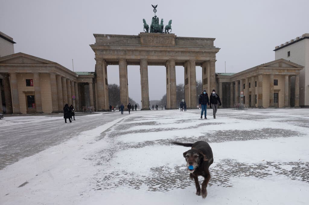 People walk with a dog on the Pariser Platz in front of the Brandenburg Gate during snowfall in central Berlin, Germany, Sunday, Feb. 7, 2021. A snowstorm and strong winds pounded parts of Germany on Sunday. (AP Photo/Markus Schreiber)
