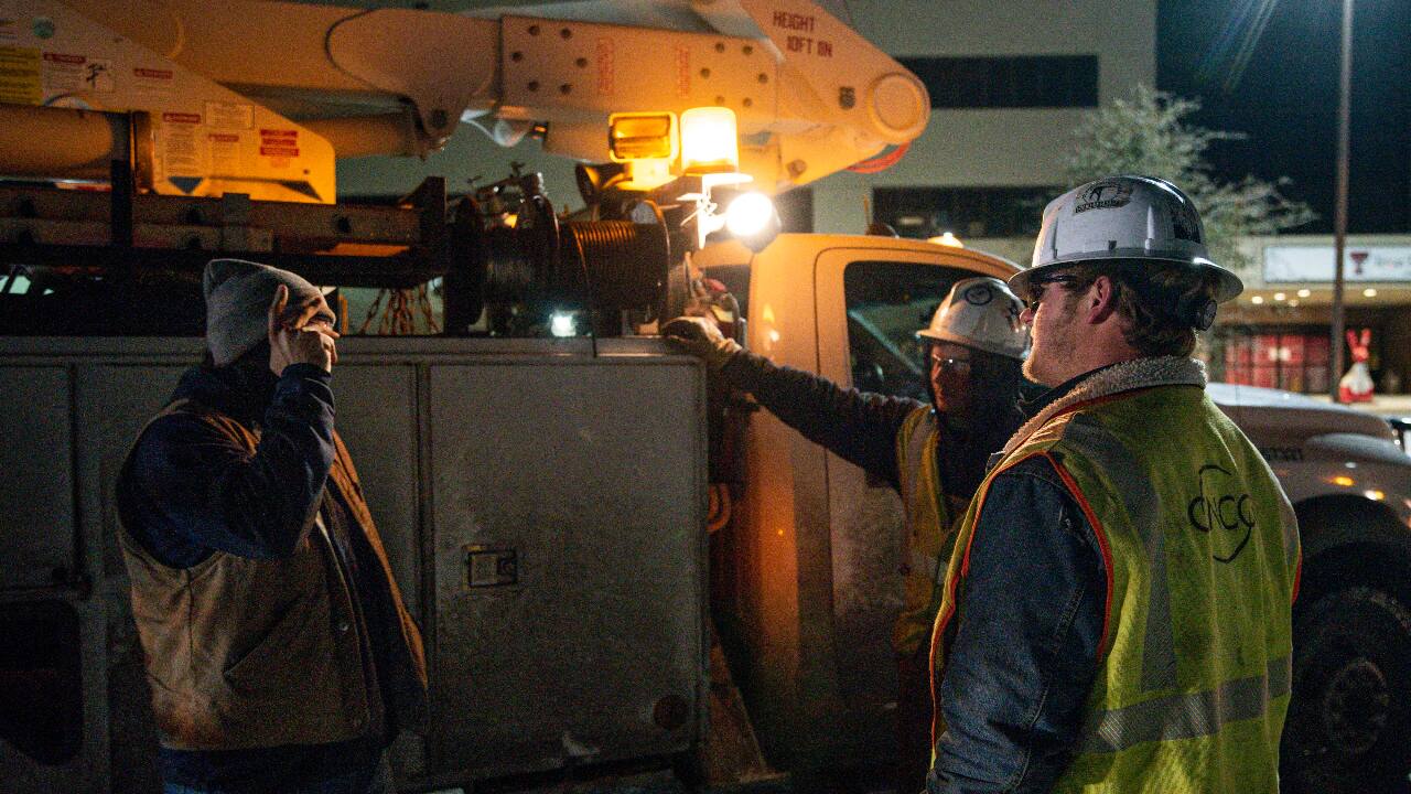 Power was restored to more homes and businesses on Thursday in states hit by a deadly blast of winter that overwhelmed the electrical grid and left millions shivering in the cold this week. Oncor Electric Delivery linemen Brendan Waldon, left, Austin Strickland, center, and Payton Merket, right, share a conversation as they wait for a new work order after repairing a utility pole damaged by snow and ice on February 18, 2021, in Odessa, Texas. (PC-Eli Hartman/Odessa American via AP)