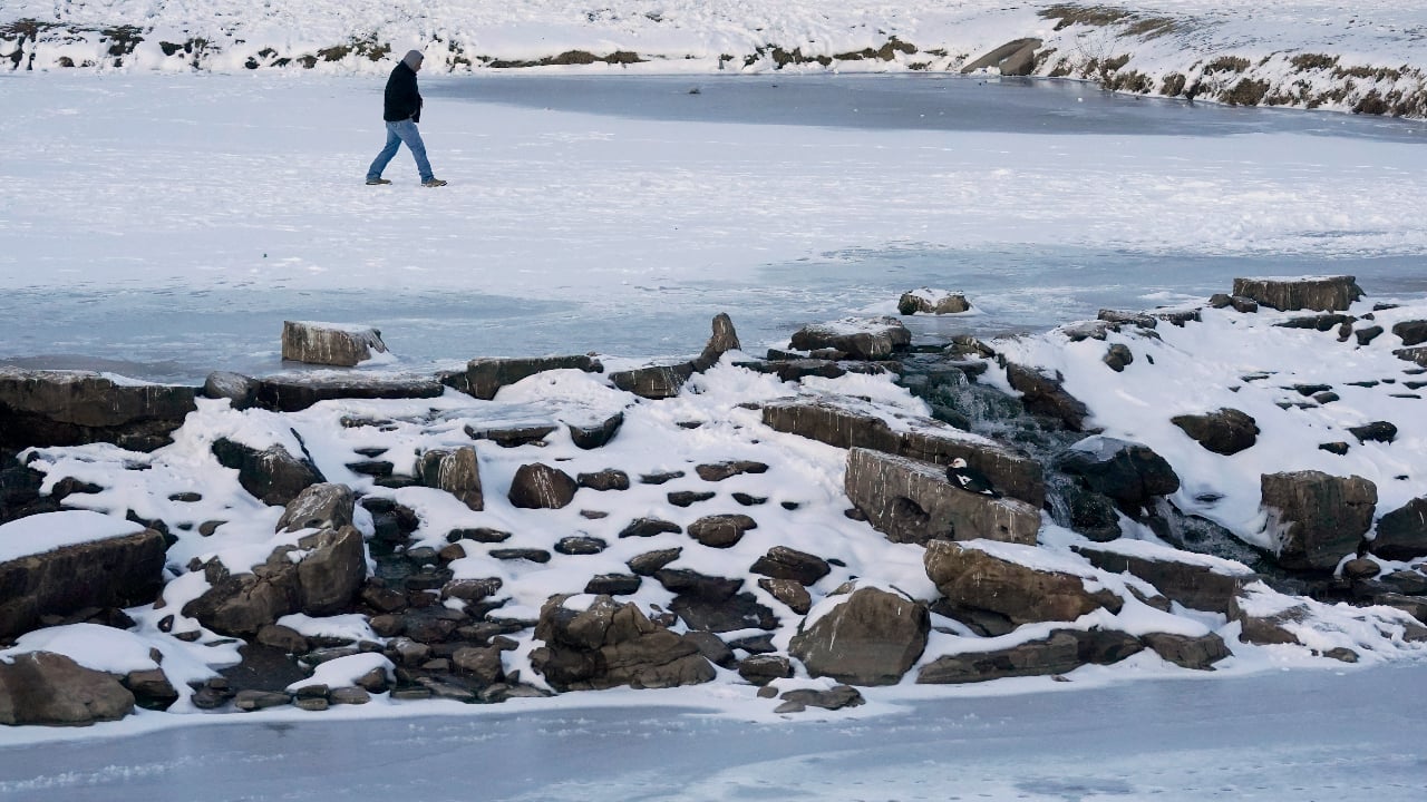 A man walks across a frozen lake at Cottonwood Park in Richardson, Texas, February. 18, 2021. Temperatures in the region continue to remain below freezing heading into Friday. (PC-AP Photo/Tony Gutierrez)