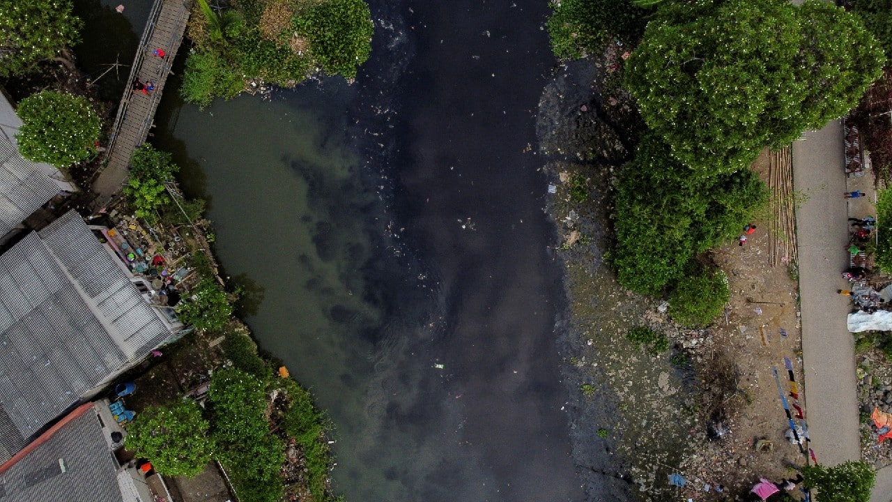 An aerial view shows people fishing from a wooden bridge at the Pisang Batu river, which flows through a densely populated area and is polluted by domestic waste, in Bekasi, on the outskirts of Jakarta, Indonesia, March 16, 2021. Pisang Batu river, on the outskirts of Jakarta, made national headlines in 2019 after plastic garbage and organic waste from nearby households completely covered its surface stretching 1.5 kilometres. The river has fewer waste after several cleanup operations, but the water is black, emitting a strong odour. (Image: Reuters)