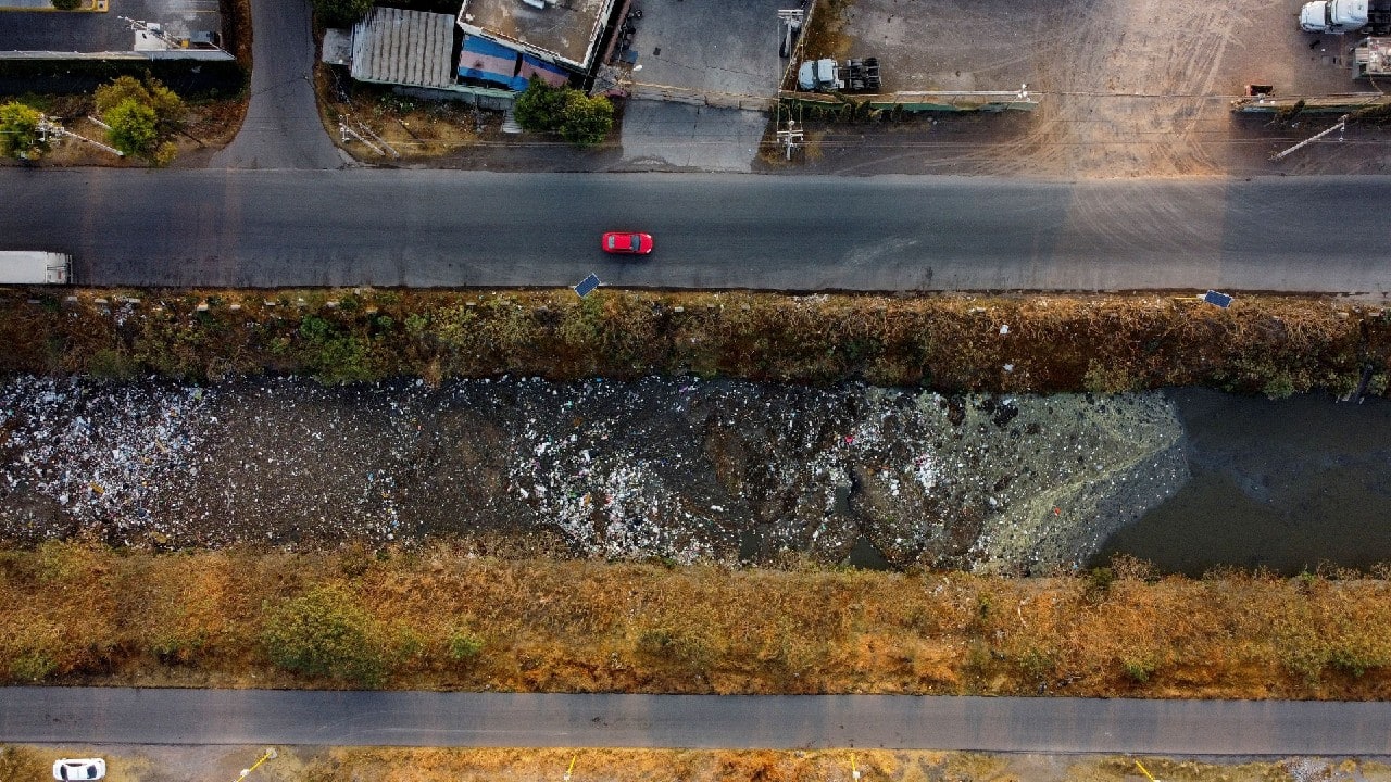 An aerial view shows cars moving next to the Interceptor Poniente canal in Cuautitlan, State of Mexico, Mexico, March 18, 2021. Drainage system waterways around densely-populated Mexico City, like the Interceptor Poniente, are heavily polluted with sewage and trash from nearby communities. Access to reliable water services is limited in low-income areas. Mexico has one of the lowest shares of its population connected to public wastewater treatment plants in the Organization for Economic Co-operation and Development, according to the agency. (Image: Reuters)