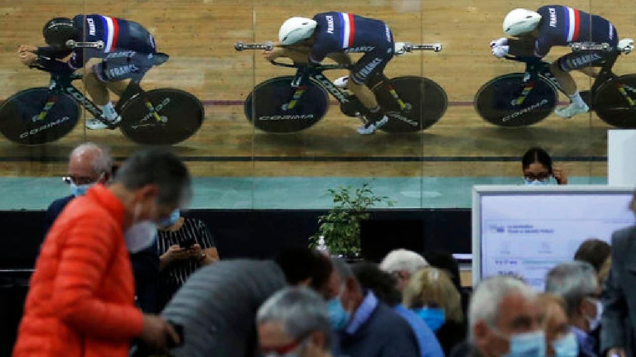 Riders of the French cycling team train as people wait for their vaccine shot at the National Velodrome that has been transformed into a mass vaccination center in Saint-Quentin-en-Yvelines, west of Paris, March 29. (Image: AP)