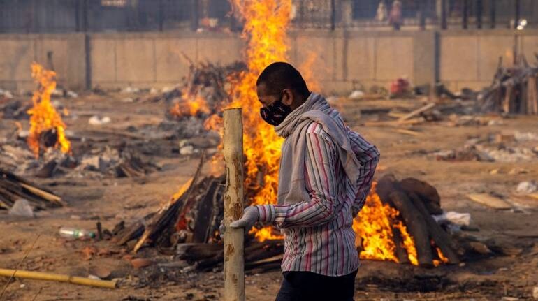 A man walks past burning funeral pyres of people, who died due to COVID-19, at a crematorium ground in New Delhi on April 22, 2021. (Image: Reuters/Danish Siddiqui)