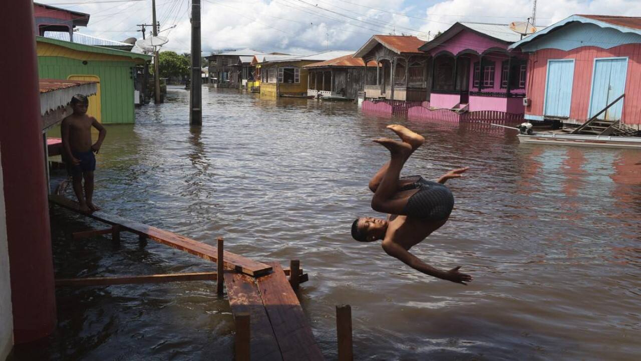A boy jumps into a flooded street in Anama, Amazonas state, Brazil, Friday, May 14, 2021. Anama, home to residents who live on a tributary of the Solimoes River that flows toward the capital Manaus, is just one municipality of dozens in Amazonas state that has seen life upended by unusual rainfall. (Image: AP)