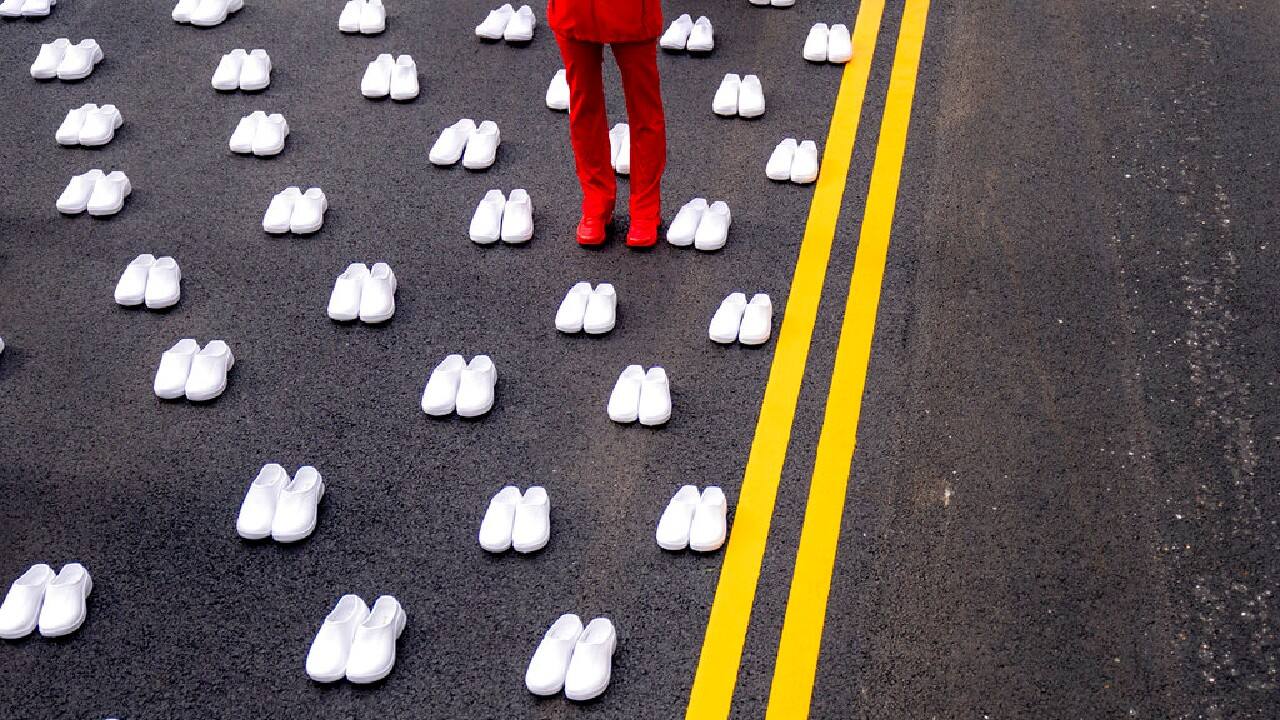 A woman in a nurses uniform stands surrounded by white pairs of shoes to represent the 402 nurses who died because of COVID-19, near the White House in Washington, May 12. National Nurses United union is asking the Biden administration to adopt Emergency Temporary Standards, which will require employers to continue to protect workers from COVID-19. (Image: AP/Andrew Harnik)