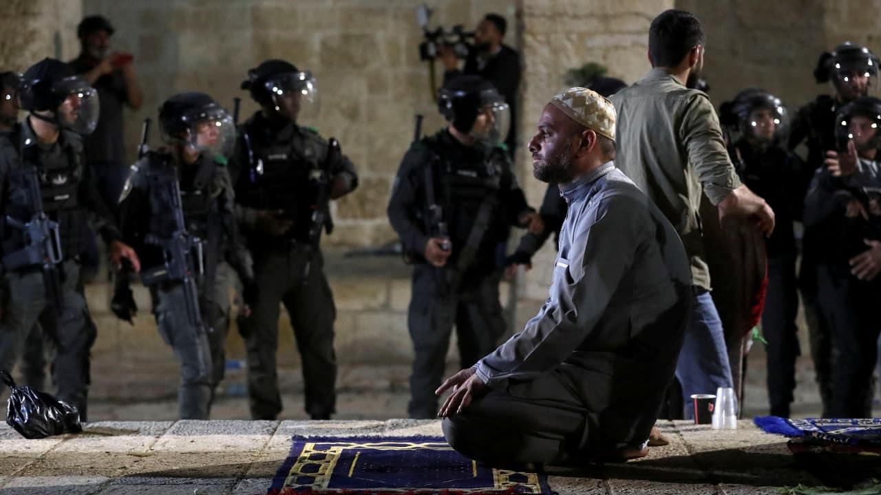 A Palestinian man prays as Israeli police gather during clashes at the compound that houses Al-Aqsa Mosque amid tension over the possible eviction of several Palestinian families from homes on land claimed by Jewish settlers in the Sheikh Jarrah neighbourhood, in Jerusalem's Old City on May 7, 2021. (Image: Reuters/Ammar Awad)