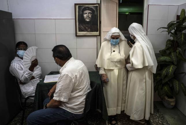 A framed image of Argentine-born Cuban revolutionary hero Ernesto &quot;Che&quot; Guevara hangs on a wall while nuns leave after being inoculated with a dose of the Cuban Abdala COVID-19 vaccine, in Havana, Cuba, Wednesday, June 23, 2021. (AP Photo/Ramon Espinosa)