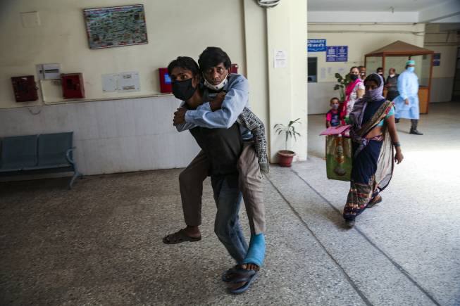 A man carries another on his back bringing him for a medical check up at a government hospital in Jammu, India, Monday, June 21, 2021. (AP Photo/Channi Anand)