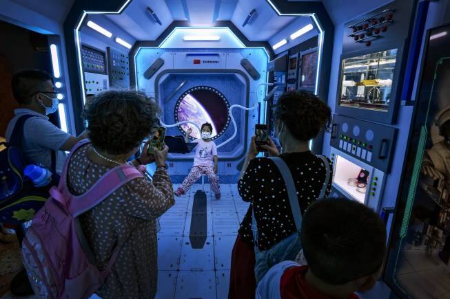 Visitors take smartphone photos of a child posing at a mock space station at an exhibition promoting China's achievements under the Communist Party from 1921 to 2021, in Beijing, Tuesday, June 22, 2021. Authorities in the capital city are gearing up to mark the 100th anniversary of the founding of China's ruling Communist Party, which will be observed on July 1. (AP Photo/Andy Wong)