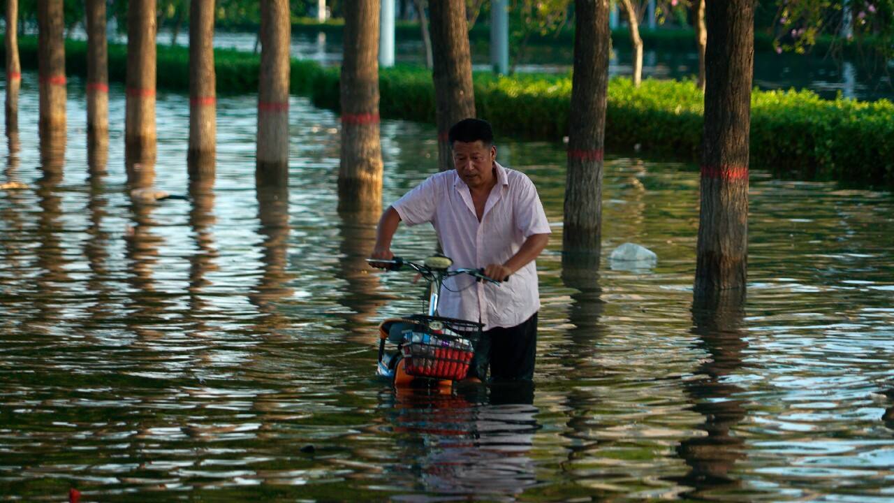 A man pushes a scooter through floodwaters in Xinxiang in central China's Henan Province, July 26. (Image: AP)